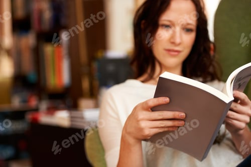 Preview: Immersed in the words. A young woman quietly reading a book while seated in a chair.