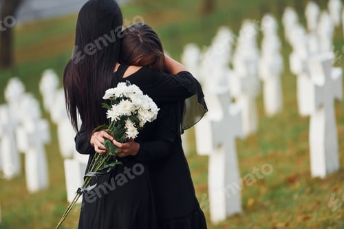 Preview: Two young women in black clothes visiting cemetery with many white crosses