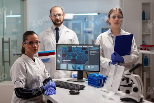 Preview: Team of scientists sitting in laboratory looking at camera in modern lab