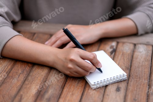 Preview: Closeup image of a woman writing on blank notebook on wooden table