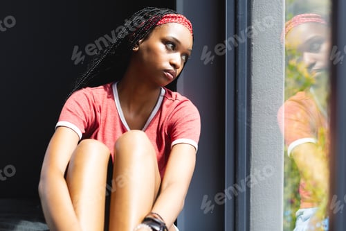 Preview: A young African American woman gazes out a window, deep in thought