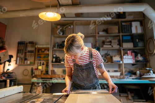 Preview: Woman carpenter inspecting wooden beam straightness with ruler before cutting with saw in workshop