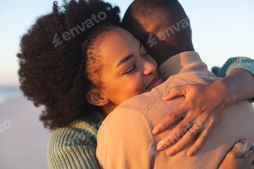 Preview: Happy african american couple embracing and smiling on sunny beach