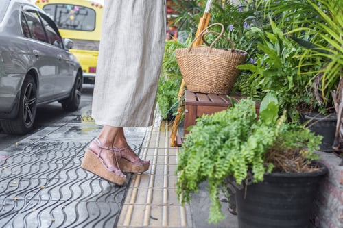 Preview: Pretty woman in beige color dress holding ratang hat and eco straw bag, walking on street