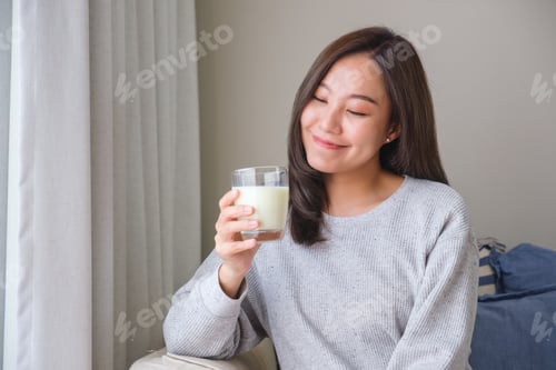 Preview: Portrait image of a young woman holding and showing a glass of fresh milk