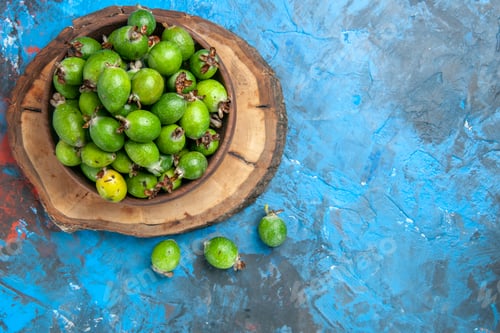 Preview: Front view of delicious vitamin bomb fresh feijoas in a brown pot on wooden tray on blue background