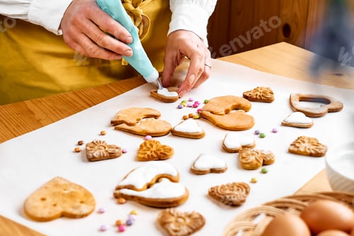 Preview: Woman decorating heart shaped cookies with frosting. Glazed festive homemade biscuits