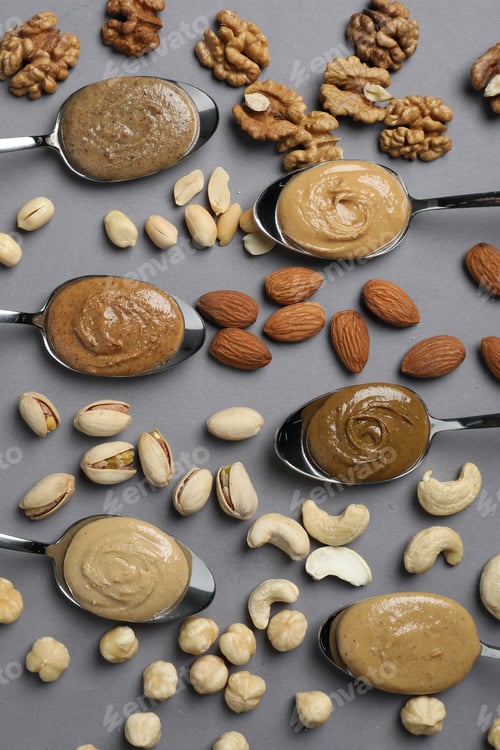 Preview: Tasty nut butters in spoons and raw nuts on gray table, flat lay