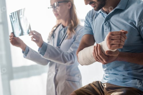 Preview: selective focus of injured man near attractive doctor looking at x-ray