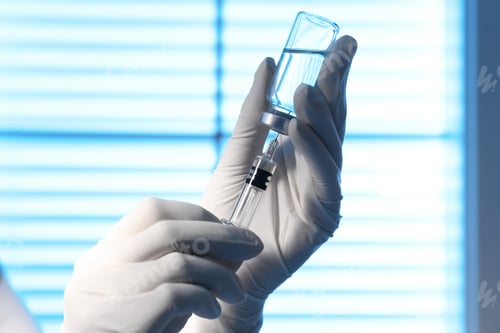 Preview: Woman filling syringe with vaccine from vial on blurred background, closeup