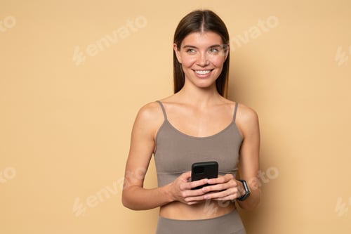 Preview: Woman fitness blogger writing post for her social media holding phone on brown studio background