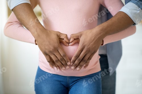Preview: Closeup view of black pregnant woman and her husband hugging tummy together, making heart with their