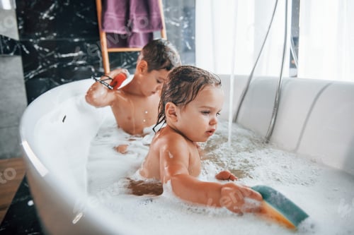 Preview: Two kids having fun and washing themselves in the bath at home. Helping each other