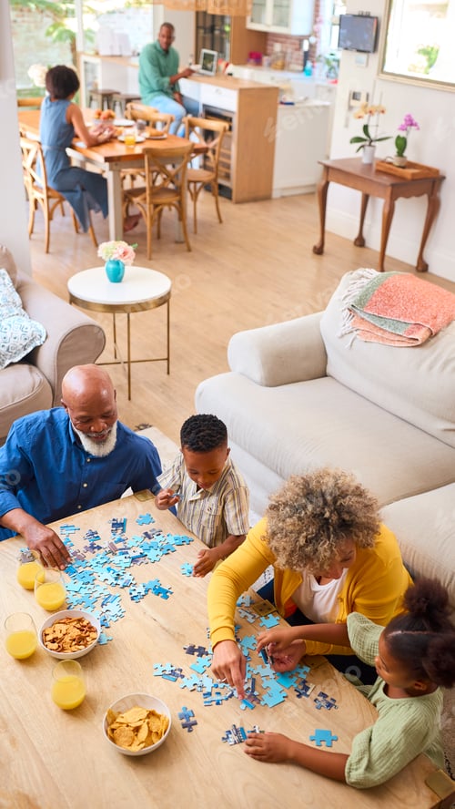 Preview: Grandparents With Grandchildren Indoors At Home Doing Jigsaw Puzzle With Parents In Background