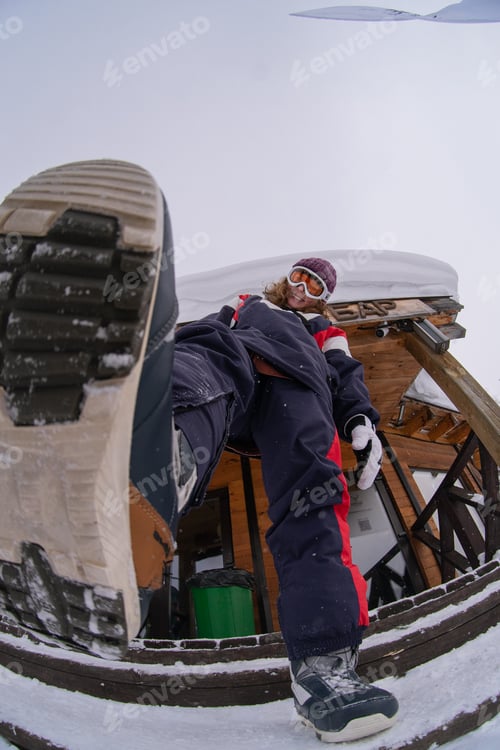 Preview: A girl at a resort in full growth with a snowboard boot in the foreground