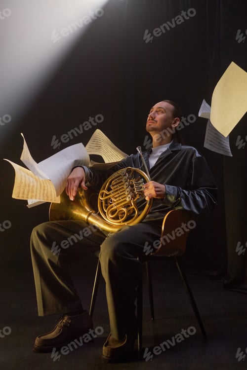 Preview: French Horn Player Sitting in Chair while Music Notes Floating around in Black Studio