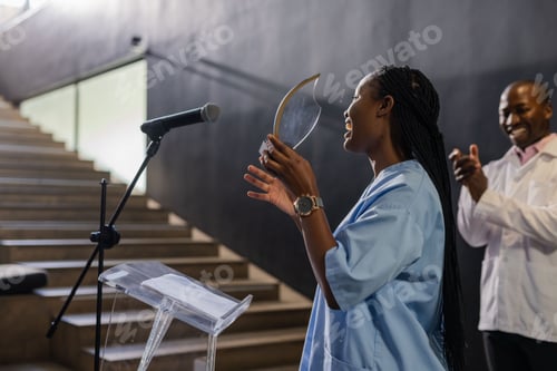 Preview: African American woman holding award, smiling and speaking at podium, man applauding