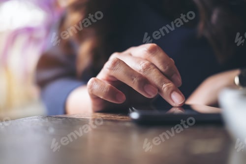 Preview: A business woman's hand touching and sliding finger on a black smart phone on wooden table