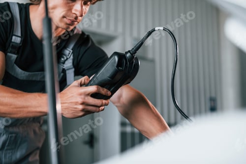 Preview: Tests car's electronics. Adult man in grey colored uniform works in the automobile salon