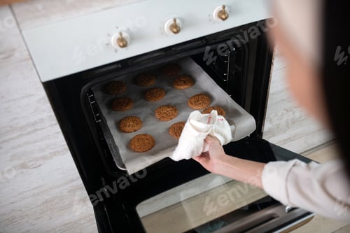 Preview: Female hand taking out baking sheet from the oven.