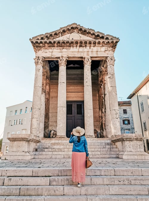 Preview: Rear view of woman walking in square of ancient town in front of ancient building in Pula, Croatia.