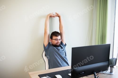Preview: man looking at computer stretching her arm after overworked relax muscle and take a break in the wor
