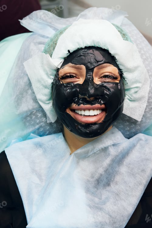 Preview: Joyful girl with alginate black mask on her face. Cosmetic rejuvenation procedure.