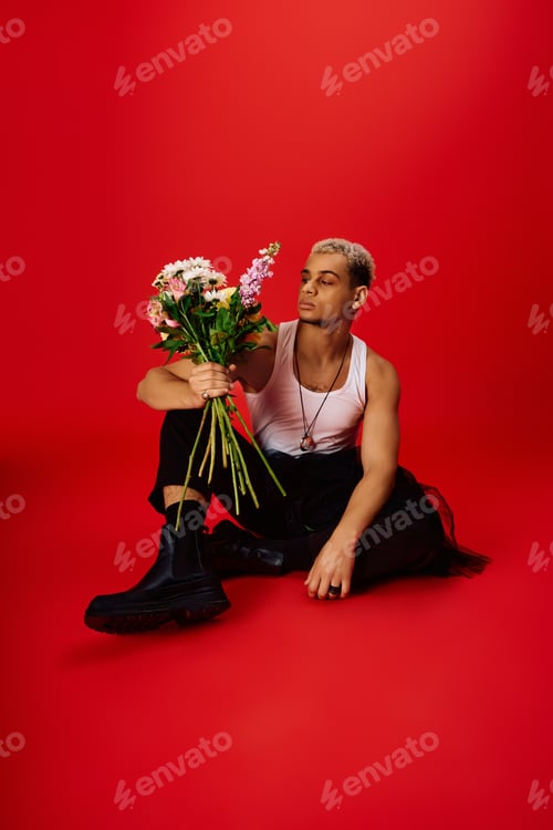 Preview: Handsome young african man with dyed hair poses with flowers in vibrant red studio