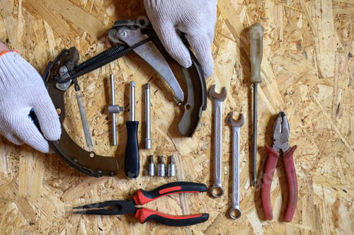 Preview: car drum brake disassembled in men's hands and a set auto mechanic's repair hand tools kit flat lay