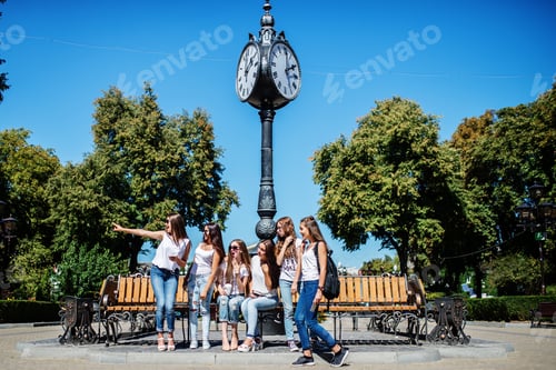Preview: Six beautiful young girls sitting on a bench next to the old street clock in the park.