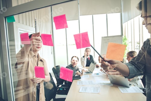 Vorschau: Geschäftsleute, die sich mit uns im Büro treffen, veröffentlichen Notizen auf einer klaren Tafel, um Ideen auszutauschen.