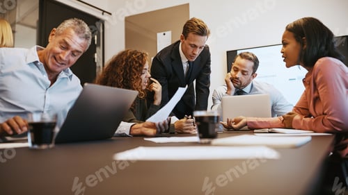 Preview: Diverse businesspeople discussing paperwork together around an office table