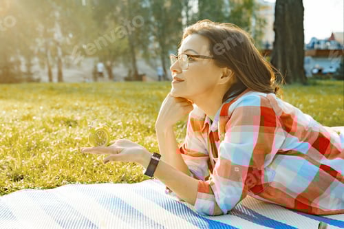 Preview: Alarm clock in female hand, background green grass in park, sunlight, copy space