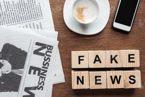 Preview: top view of wooden cubes with words fake news, cup of coffee and smartphone on wooden tabletop
