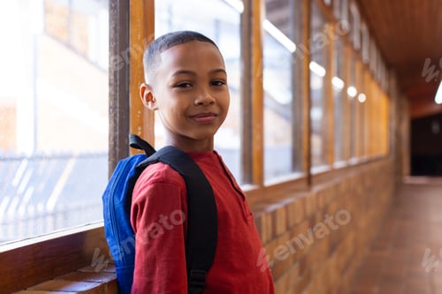 Preview: Smiling boy with backpack standing in school hallway, looking at camera