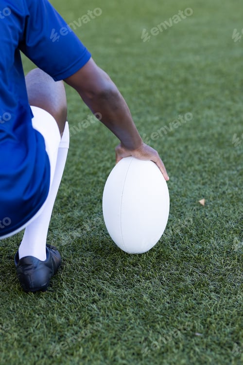 Preview: African American young male athlete holding a rugby ball on field outdoors on grass, copy space