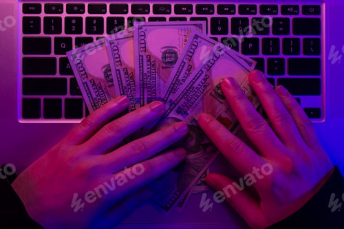 Preview: Money in male hands on the background of a laptop keyboard in neon lighting.