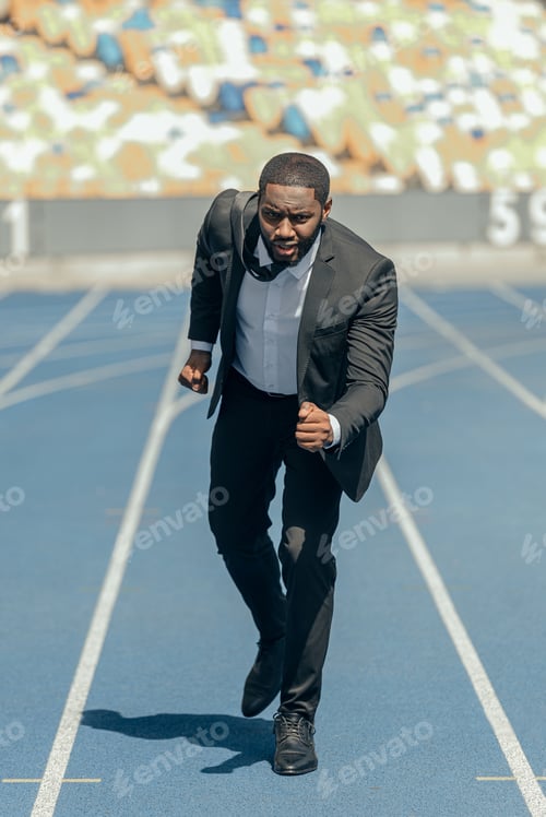 Preview: Full-length photo of African man in business suit running on sport track