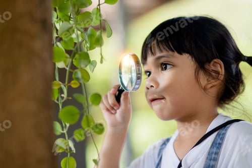 Preview: Asian little girl is looking at tree leaves through magnifier, outdoor shoot