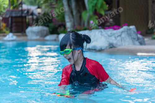 Preview: Asian little girl in swimsuit playing with toys at swimming pool happily and having fun.