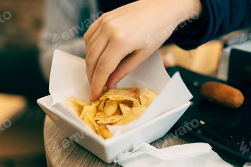 Preview: Selective focus shot of a person taking chips from a bowl