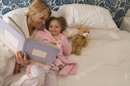 Preview: High angle view of happy mother with her young daughter reading storybook in bedroom at home