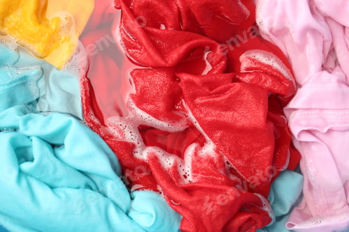Preview: Colorful clothes soaked in water before washing, top view