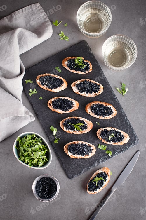 Preview: Toasts with black caviar and two glasses of white wine on grey stone background