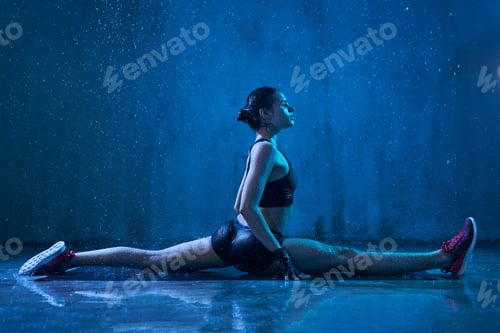 Preview: Fitnesswoman practicing split under rain