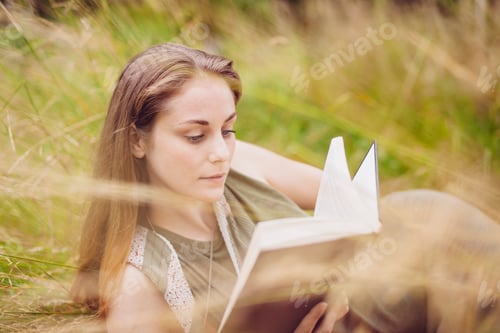 Preview: Young woman sitting in long grass reading book