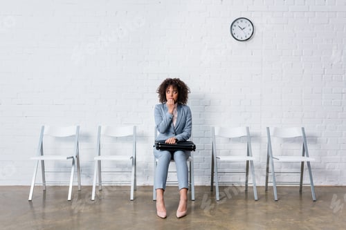 Preview: Stressed woman in suit sitting on chair with briefcase and waiting