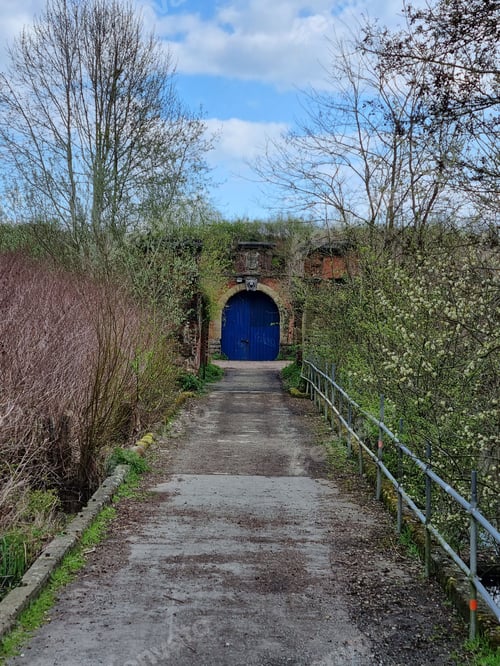Preview: Majestic view of historical Fort 3 in Belgium, with a blue door against a cloudy blue sky