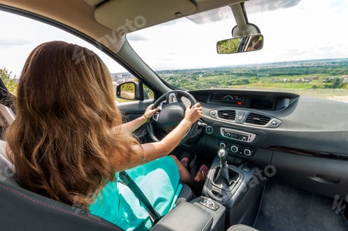 Preview: Girl in dress with red hair driving a car. Rear view