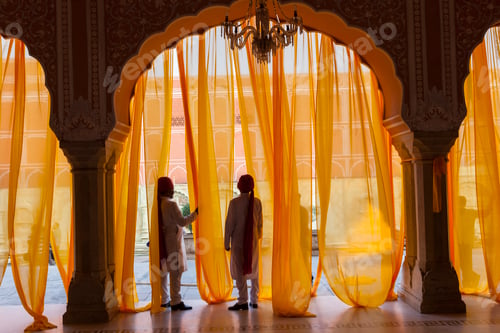 Preview: Two men under arch decorated with translucent orange curtains.